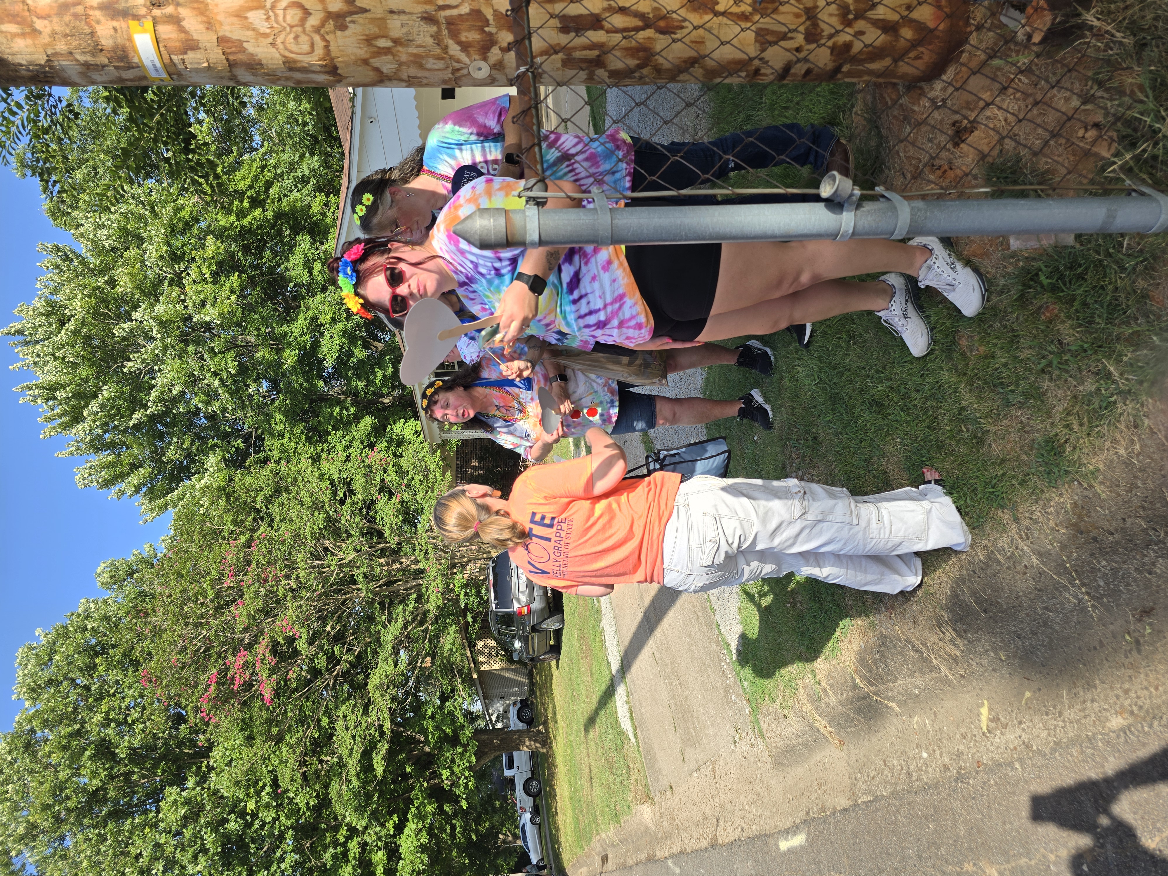 Kelly Grappe in a Vote Kelly Grappe for Secretary of State shirt talks with festival-goers in tie-dye along a sunny street.
