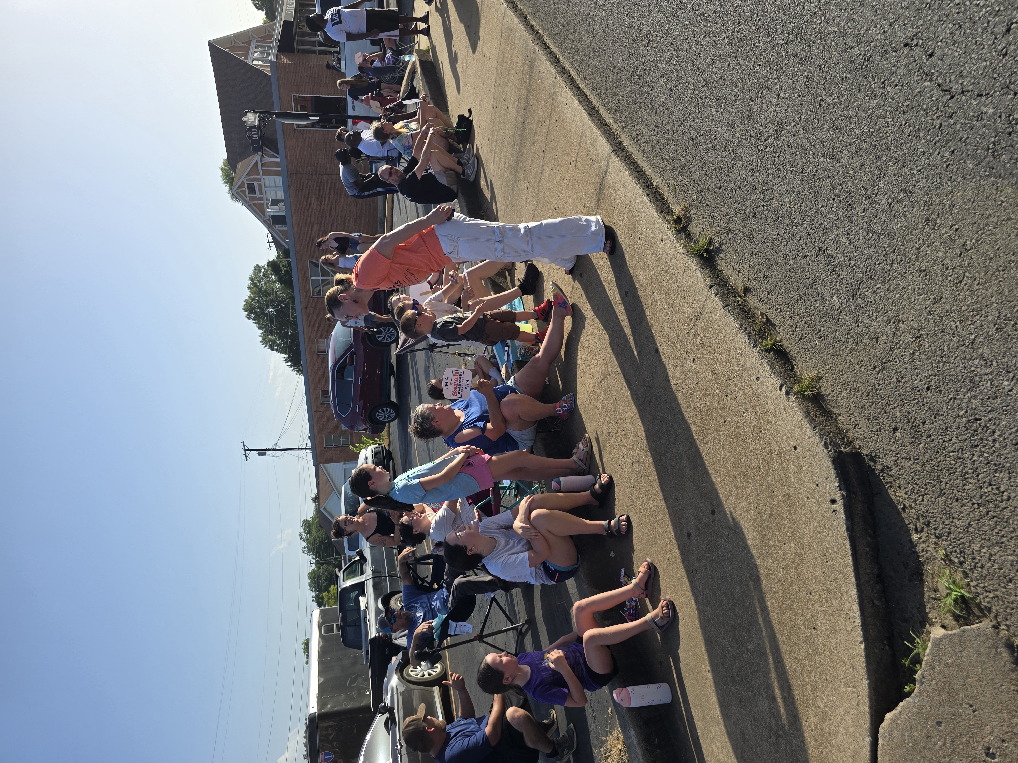 Kelly Grappe in Johnson, Arkansas — campaign photo Kelly Grappe kneels to speak with children and families seated on a curb during a sunny community festival. Johnson, Arkansas.
