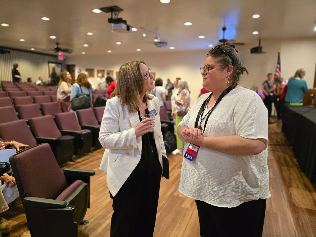 Kelly Grappe for Arkansas Secretary of State — campaign photo Kelly Grappe, candidate for Arkansas Secretary of State. Kelly Grappe talks with a credentialed attendee on an auditorium floor beside theater seating.