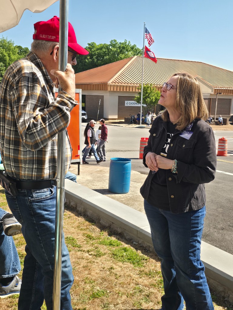 Kelly Grappe for Arkansas Secretary of State — campaign photo Kelly Grappe, candidate for Arkansas Secretary of State. Kelly Grappe talks with a community member outdoors near a Cadence Bank building.