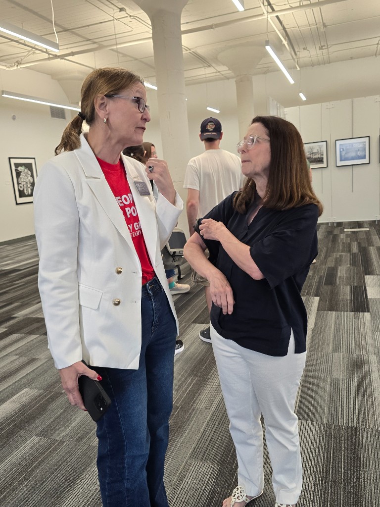 Kelly Grappe for Arkansas Secretary of State — campaign photo Kelly Grappe, candidate for Arkansas Secretary of State. Kelly Grappe talks with a community member in a bright indoor gallery space.