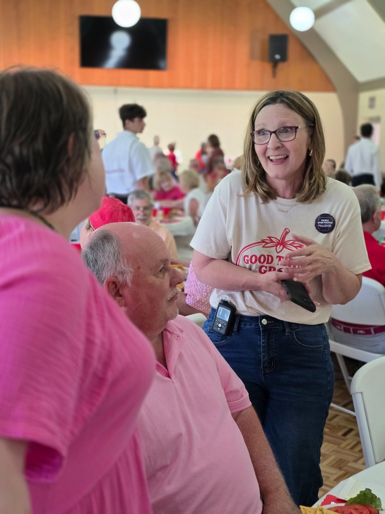 Kelly Grappe for Arkansas Secretary of State — campaign photo Kelly Grappe, candidate for Arkansas Secretary of State. Kelly Grappe talks with seated community members at a Good Things Grow hall meal.