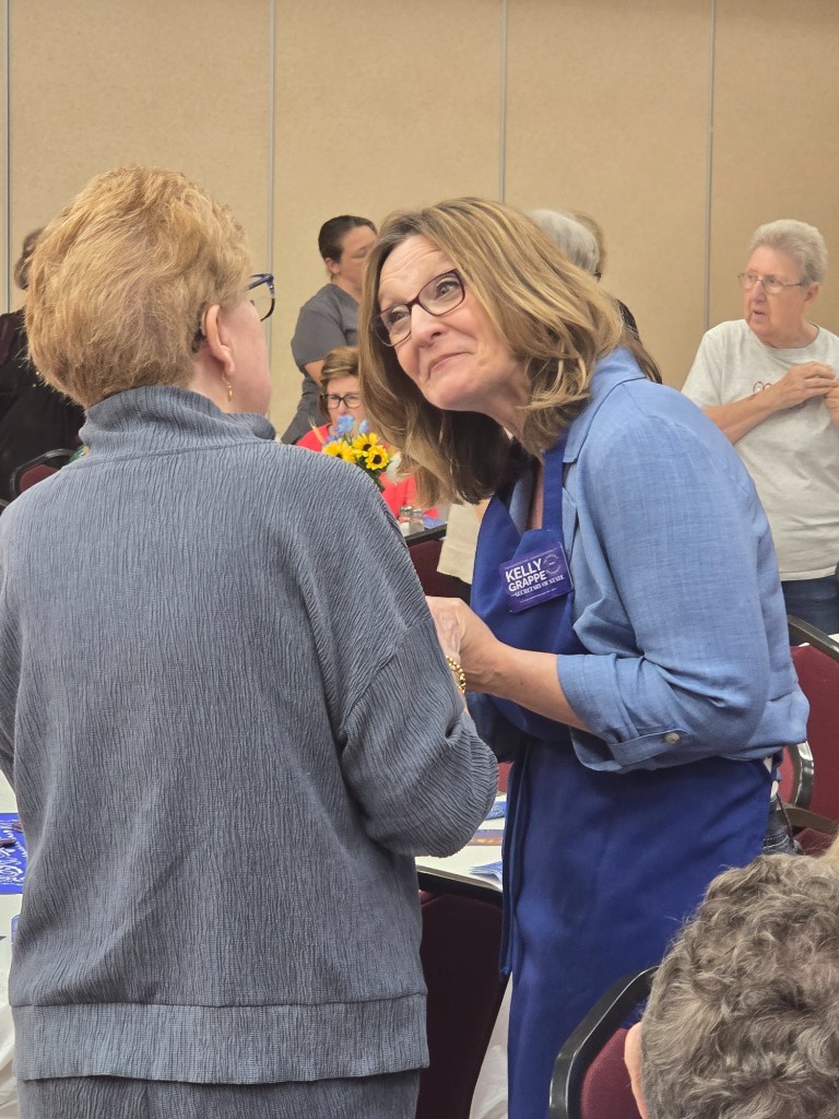 Kelly Grappe for Arkansas Secretary of State — campaign photo Kelly Grappe, candidate for Arkansas Secretary of State. Kelly Grappe listens to a community member during an indoor hall gathering.