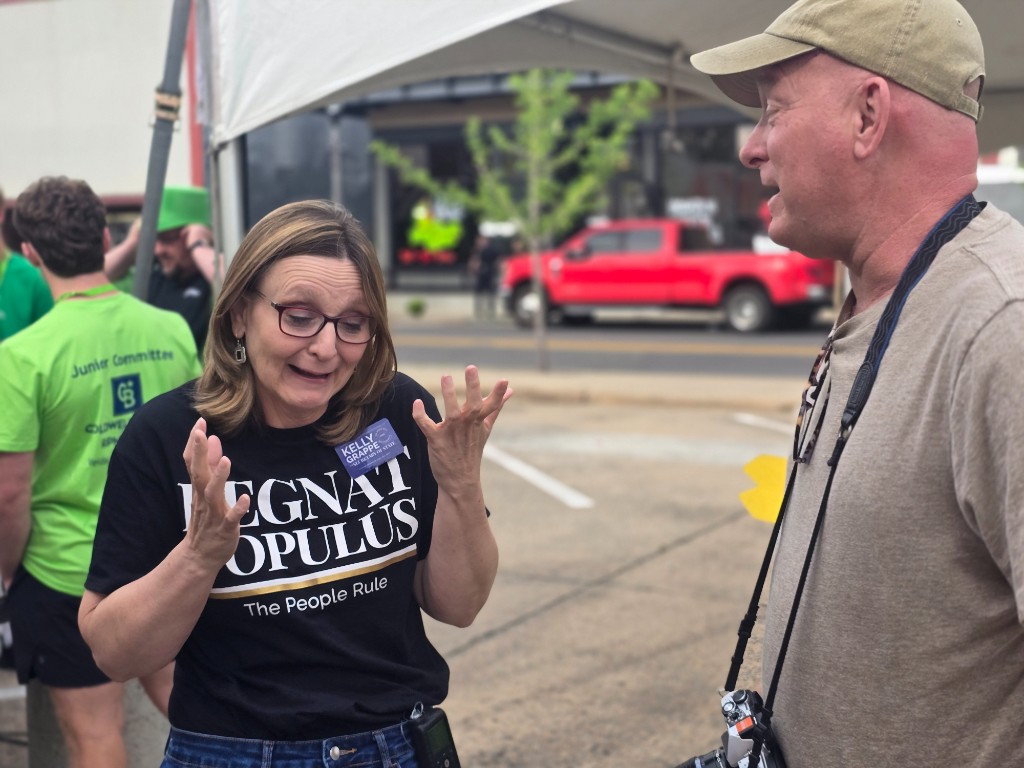 Kelly Grappe for Arkansas Secretary of State — campaign photo Kelly Grappe, candidate for Arkansas Secretary of State. Kelly Grappe in a Regnat Populus shirt talks with a festival-goer under a tent.
