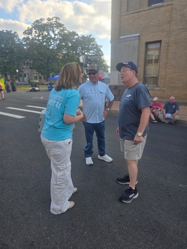 Kelly Grappe for Arkansas Secretary of State — campaign photo Kelly Grappe, candidate for Arkansas Secretary of State. Kelly Grappe talks with neighbors on a downtown street while wearing a Vote campaign shirt.
