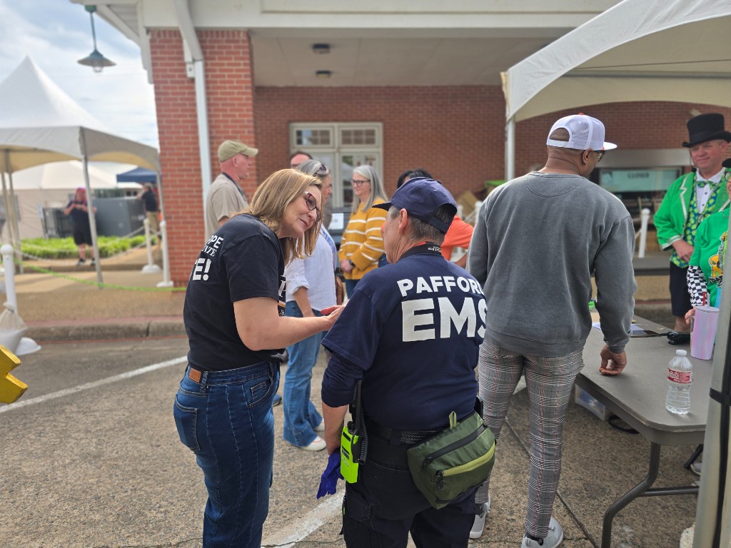 Kelly Grappe in Faulkner, Arkansas — campaign photo Kelly Grappe in a campaign shirt talks with a Pafford EMS first responder at an outdoor festival. Faulkner, Arkansas.