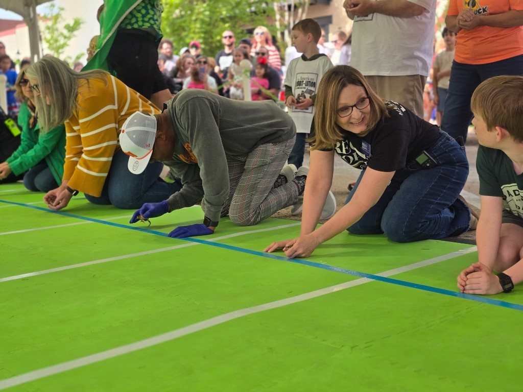 Kelly Grappe kneels on a green mat at the starting line of a toad race, smiling beside other participants.