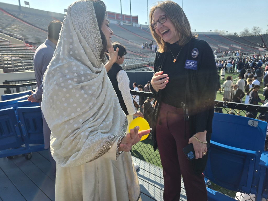 Kelly Grappe in Pulaski, Arkansas — campaign photo Kelly Grappe laughs with a community member in traditional attire at War Memorial Stadium during a large field celebration. Pulaski, Arkansas.